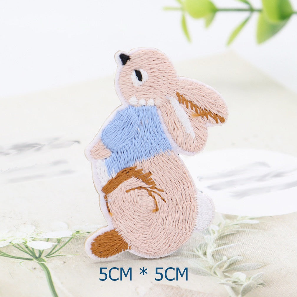 Left-facing seated bunny embroidered patch with a blue jacket and long ears trailing right
