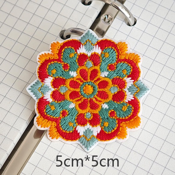 Ornamental floral embroidered stick-on patch with golden-orange stitching and teal scrolls
