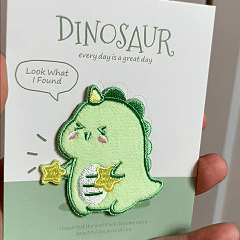 animated hand holding packaged cute dinosaur embroidered patches showing detailed embroidery texture