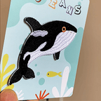 animated hand holding packaged ocean animals embroidered patches showing three styles and detailed embroidery texture
