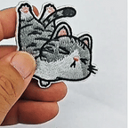 animated hand holding packaged funny everyday tabby cat embroidered patches showing multiple styles and detailed embroidery texture
