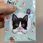 animated hand holding packaged tuxedo cat realistic cat breed embroidered patch showing detailed embroidery texture