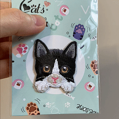 animated hand holding packaged tuxedo cat realistic cat breed embroidered patch showing detailed embroidery texture