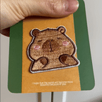 animated hand holding packaged derpy capybara embroidered patches showing two styles and detailed embroidery texture