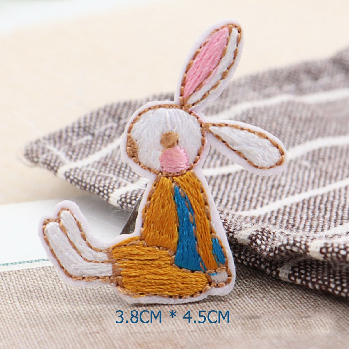 Seated white bunny embroidered patch wearing a mustard outfit over a blue top
