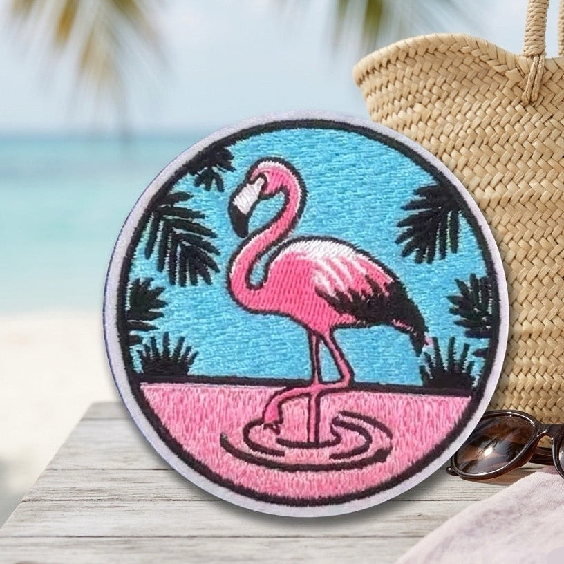 tropical flamingo embroidered stick-on patch round badge design on beach table with straw bag and sunglasses