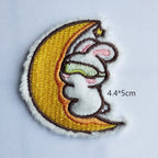 sleeping bunny on golden crescent moon embroidered stick-on patch — white bunny wearing green sleep mask curled on moon with small star at tip 44x50mm