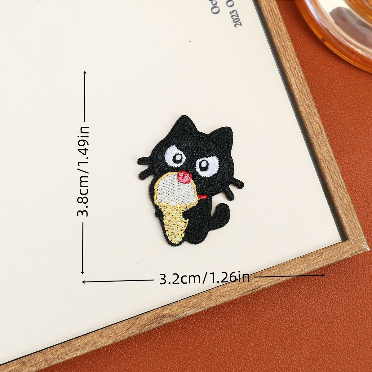 Black cat embroidered stick-on patch holding a cream-colored ice cream cone with pink topping
