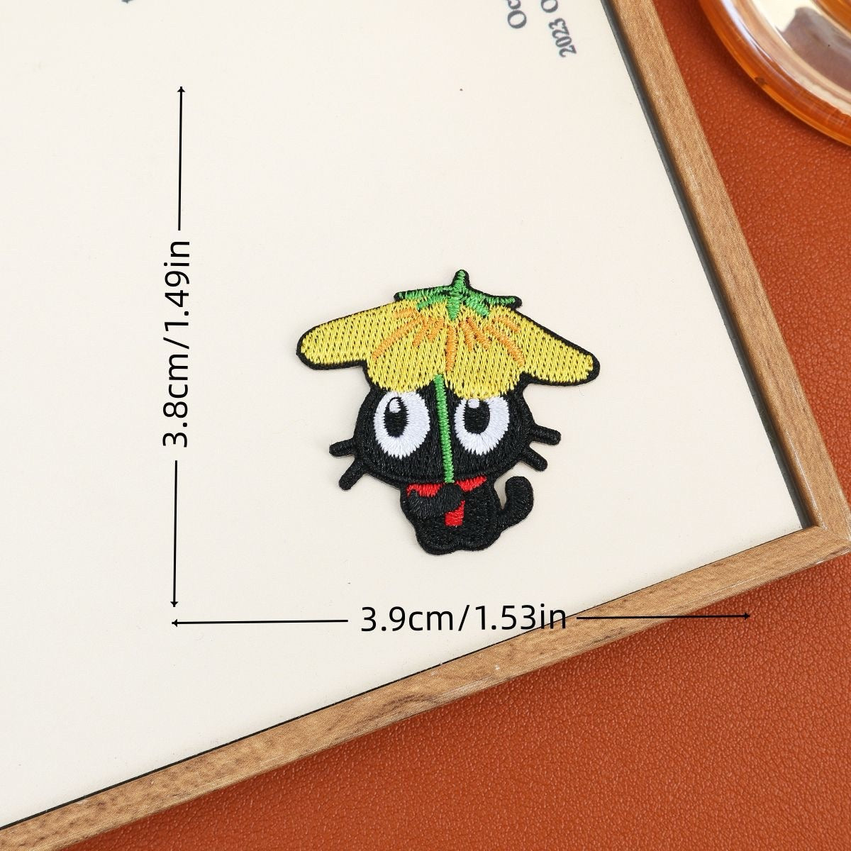 Black cat embroidered stick-on patch beneath a yellow flower-shaped umbrella with a green stem
