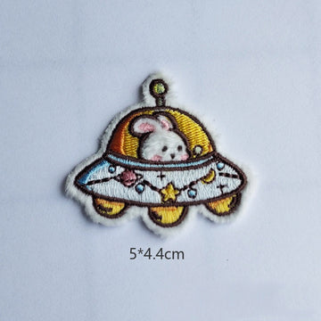 bunny in UFO embroidered stick-on patch — white bunny peering from gold dome flying saucer with star and moon decorations across disc antenna on top 50x44mm