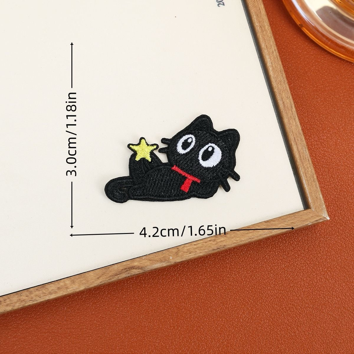 Reclining black cat embroidered stick-on patch with a red scarf and small yellow star
