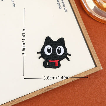 Wide-eyed sitting black cat embroidered stick-on patch with a tucked tail and red scarf
