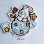 bunny on ringed planet embroidered stick-on patch — white bunny sprawled on blue saturn-ring planet with pink rose and gold stars largest of the twelve 60x56mm
