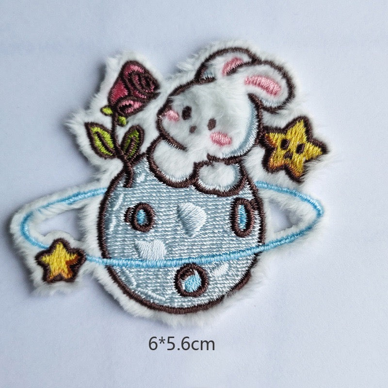 bunny on ringed planet embroidered stick-on patch — white bunny sprawled on blue saturn-ring planet with pink rose and gold stars largest of the twelve 60x56mm
