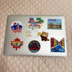 Vintage travel and world landmark embroidered stick-on patches decorating a silver laptop lid