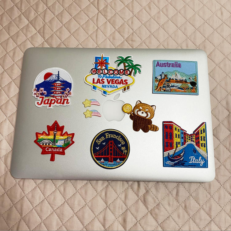 Vintage travel and world landmark embroidered stick-on patches decorating a silver laptop lid