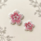 Large and small pink-and-white cherry blossom embroidered patches on an ivory background with soft botanical shadows

