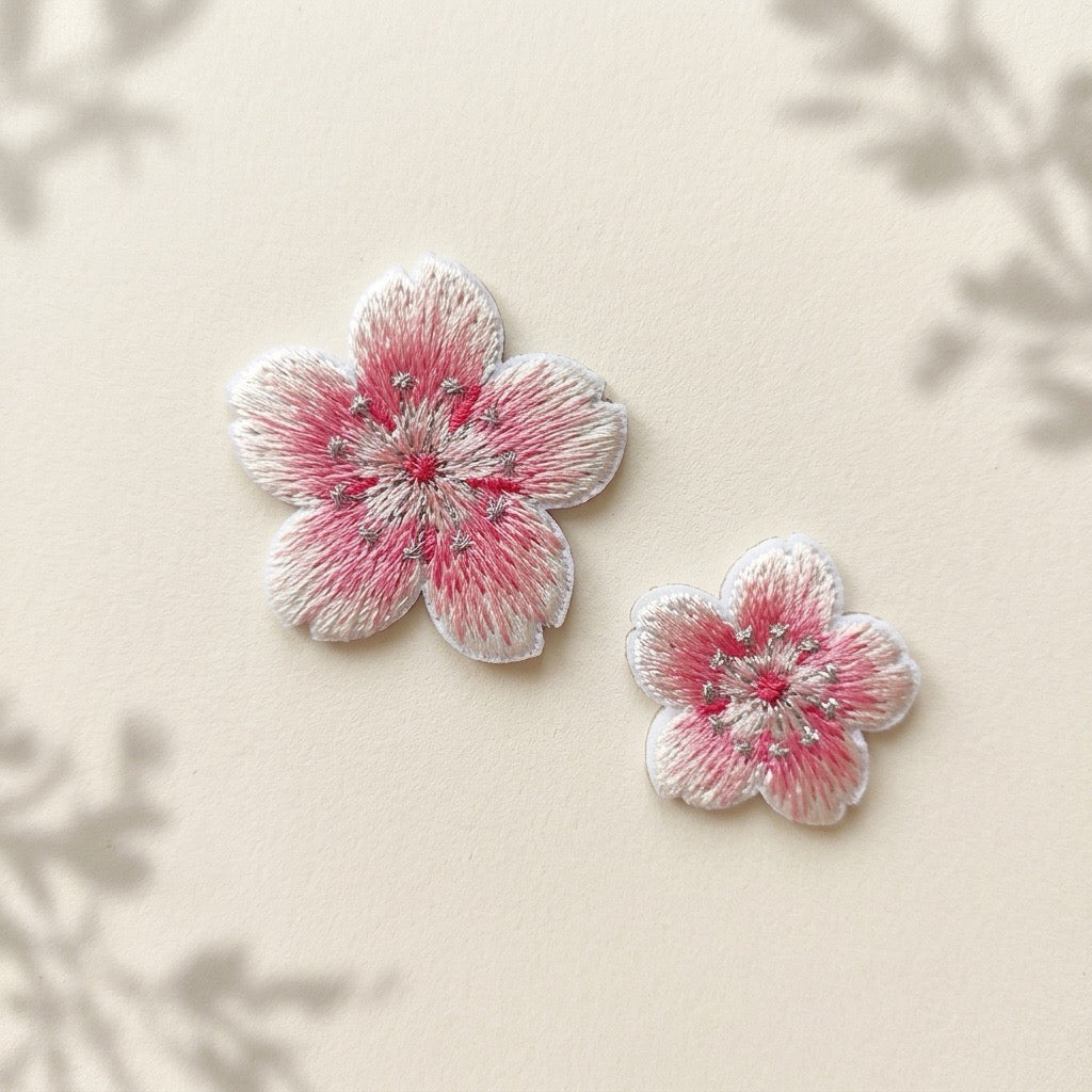 Large and small pink-and-white cherry blossom embroidered patches on an ivory background with soft botanical shadows
