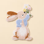 Blue-jacket bunny embroidered patch raising a flower bouquet against a warm ivory background
