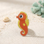cute sea creatures embroidered stick-on patches on sand — grey shark pink anglerfish blue jellyfish purple octopus red crab and orange seahorse