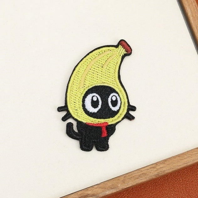 Playful black cat embroidered stick-on patch with a yellow banana hood and bright red scarf
