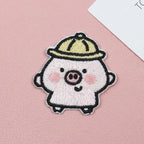 Chubby pink piglet embroidered stick-on patch wearing a yellow hat on a pink background

