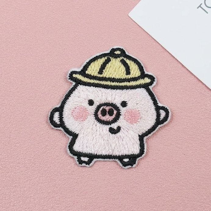 Chubby pink piglet embroidered stick-on patch wearing a yellow hat on a pink background
