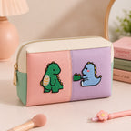 green and blue dino stick-on patches decorating a pink and purple color-block leather makeup bag