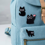 three big-eyed black cat embroidered patches on a light blue canvas backpack