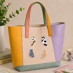 calico tabby grey and orange cat sitting back view stick-on patches decorating a yellow and purple color-block leather handbag