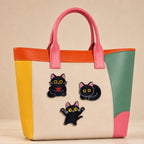black cat with pink ears holding heart curled up and jumping stick-on patches decorating a pink and orange color-block leather handbag
