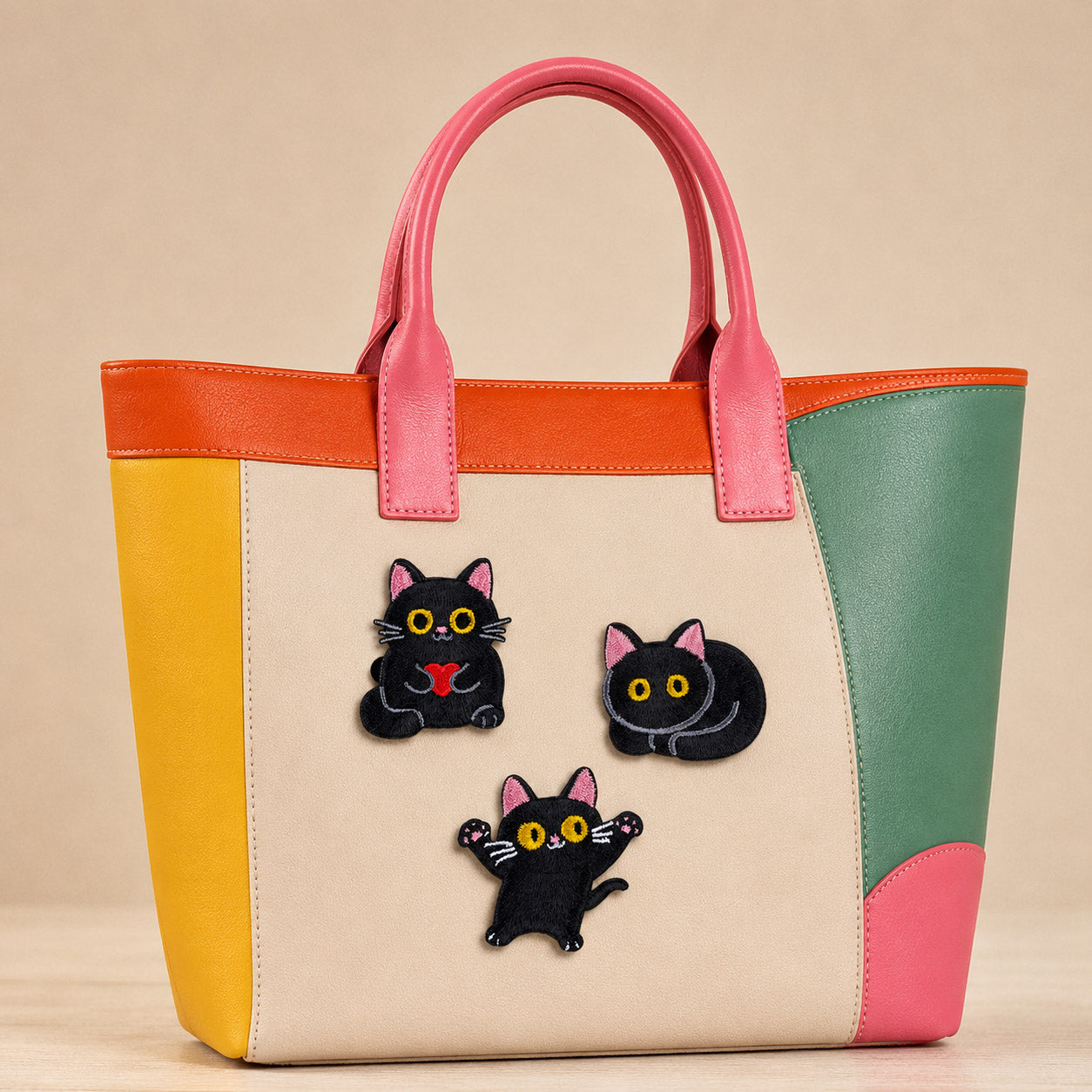 black cat with pink ears holding heart curled up and jumping stick-on patches decorating a pink and orange color-block leather handbag