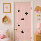 minimalist black cat silhouette stick-on patches with oversized white eyes in five poses scattered on a pink framed door in a neutral pastel bedroom