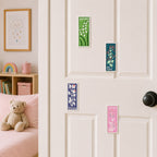 four vintage floral stamp embroidered patches in green teal navy and pink stuck on a white door in a pink kids room