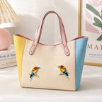two colorful bee-eater bird embroidered patches with red orange yellow and blue plumage perched on branches on a cream yellow and blue colorblock tote bag