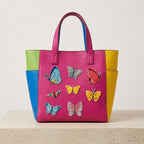seven colorful butterfly patches in blue red yellow and green on the front of a bold color-block leather tote