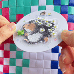 animated peel and stick demo of hedgehog holding lucky clover embroidered patch applied to a woven bag