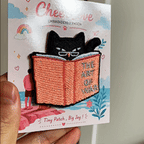 animated hand holding packaged black cat reading art of war student daily life embroidered patch showing detailed embroidery texture