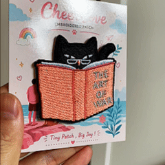 animated hand holding packaged black cat reading art of war student daily life embroidered patch showing detailed embroidery texture