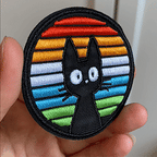 animated hand holding packaged round rainbow window black cat embroidered patch showing detailed embroidery texture