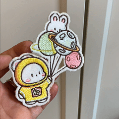 animated hand holding packaged cute space bunny embroidered patches showing multiple styles and detailed embroidery texture