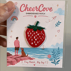 animated hand holding packaged red strawberry embroidered patches showing detailed embroidery texture