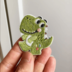 Animated hand holding four kawaii pastel dinosaur embroidered stick-on patches
