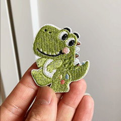 Animated hand holding four kawaii pastel dinosaur embroidered stick-on patches
