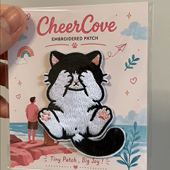 animated hand holding packaged tuxedo cat embroidered patches showing detailed embroidery texture
