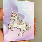 animated hand holding packaged pastel unicorn embroidered patch showing detailed embroidery texture