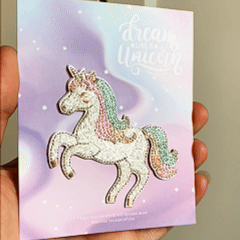 animated hand holding packaged pastel unicorn embroidered patch showing detailed embroidery texture