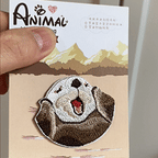 animated hand holding packaged cheering otter embroidered patch showing detailed embroidery texture