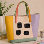 four dark aesthetic icon embroidered patches on a pastel yellow and purple color-block leather tote bag